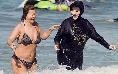 [A photo of Nigella Lawson in a black burqini cavorting in the surf with her friend Maria McErlane (who is wearing a bikini).]